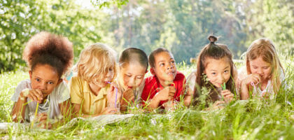 Children drink water with straw on meadow